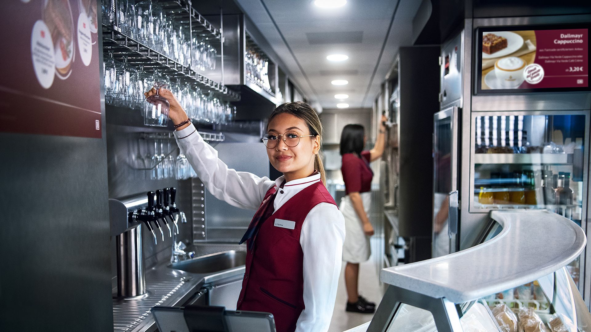 Eine Auszubildende Fachfrau für Systemgastronomiesteht in Unternehmensbekleidung im Bordbistro und zapft ein Getränk